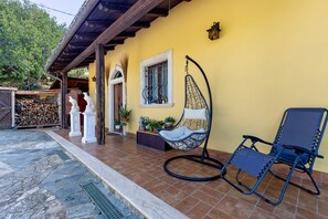 A yellow building with a covered patio area, a hanging chair, and a blue lounge chair.