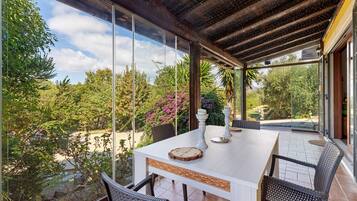 A covered outdoor dining area with a table, chairs, and a view of the surrounding garden.