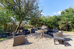 An outdoor seating area with wicker furniture and a stone table, surrounded by gravel and trees.