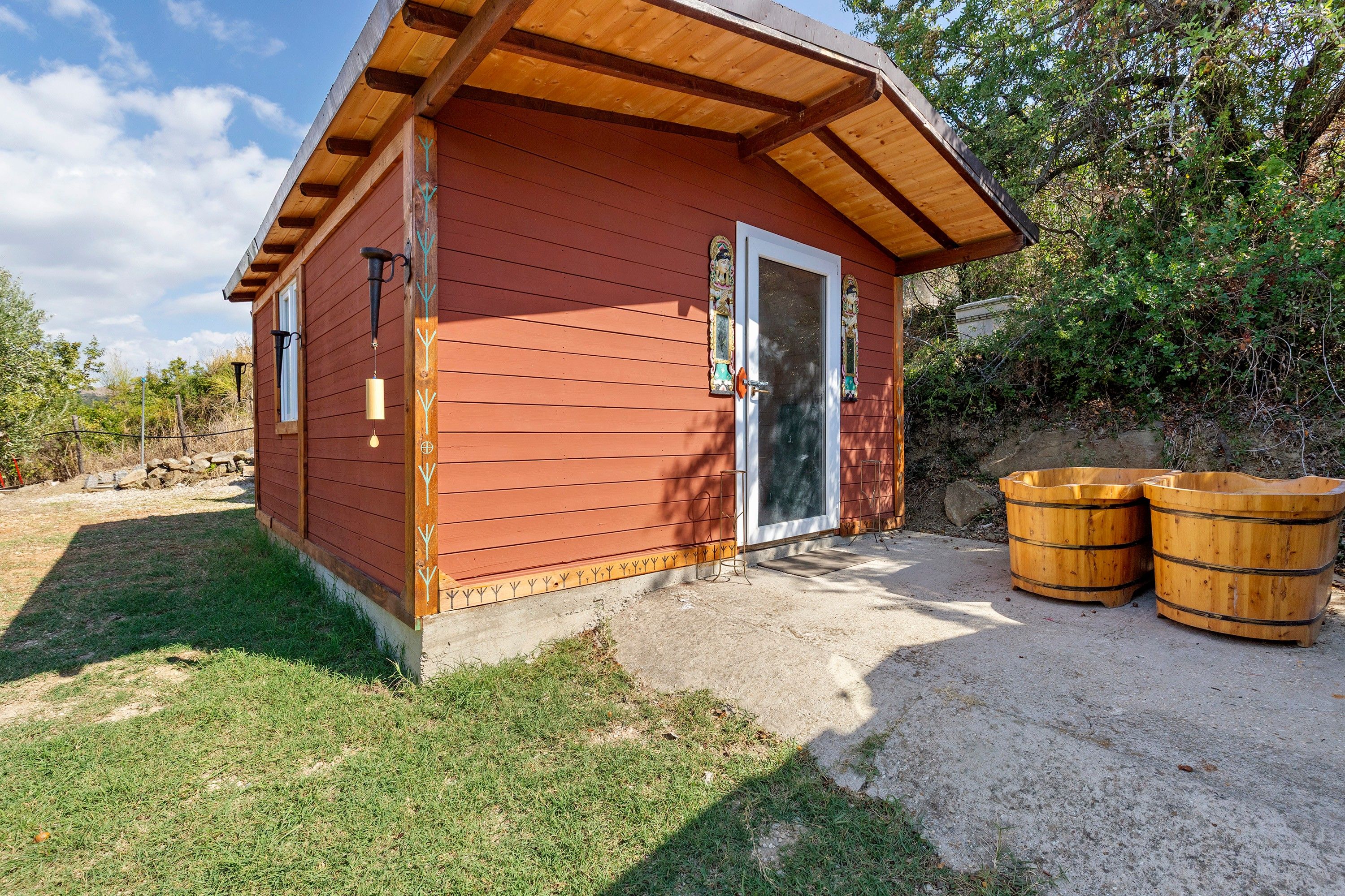Eine kleine Holzhütte mit geneigtem Dach, einer Glastür und zwei Holzfässern vor der Tür.