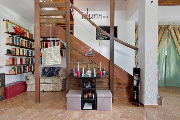 A room with a wooden staircase, a bookshelf filled with books, a small table with decorative items, and a sign on the wall.