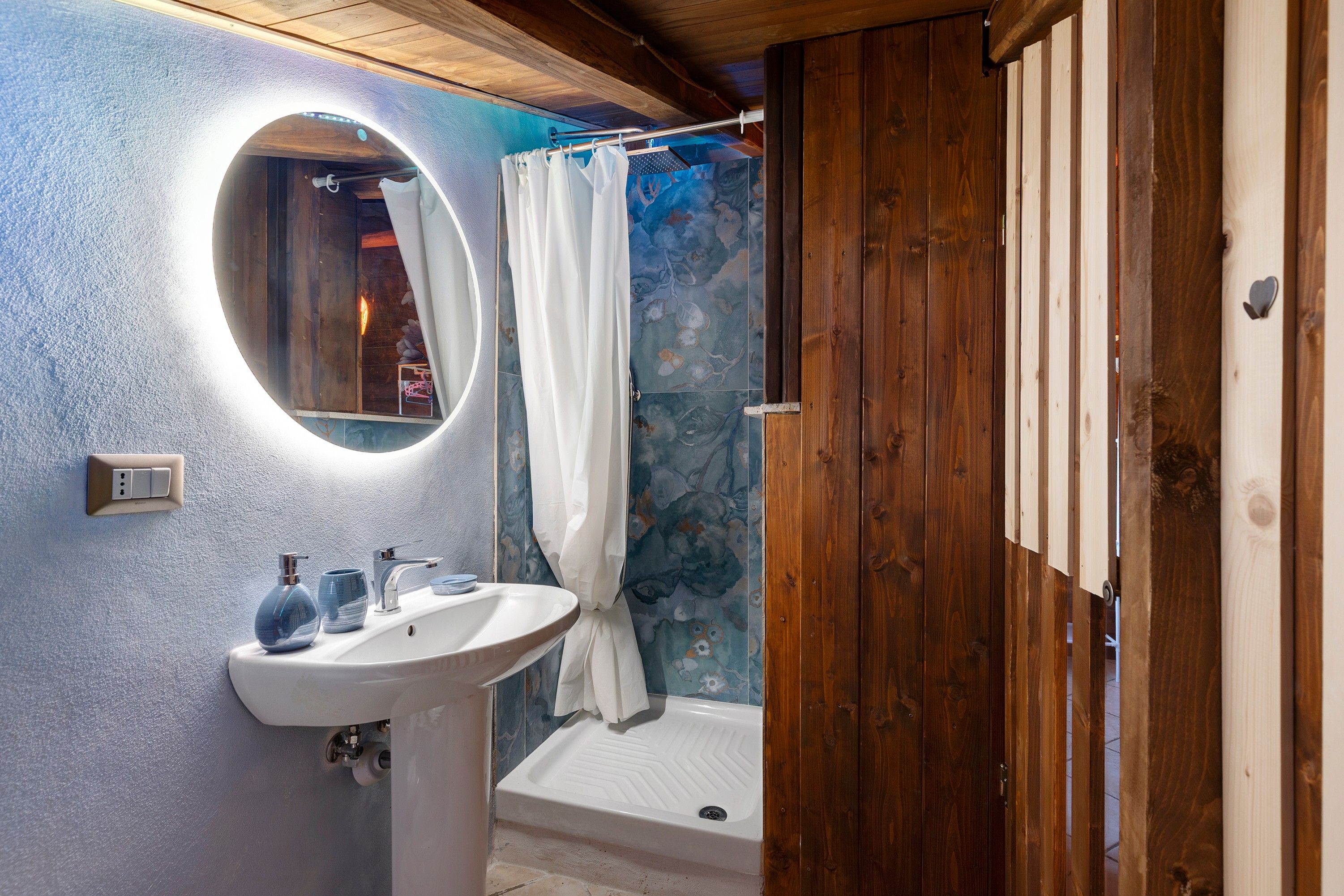 A bathroom with a white sink, a mirror, a shower curtain, and a wooden door.