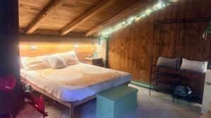 A cozy bedroom with a wooden ceiling, a bed with patterned bedding, a bedside table, and a green bench. - Room 'Terra' with shared pool, Wi-Fi and air conditioning (Santa Marinella)