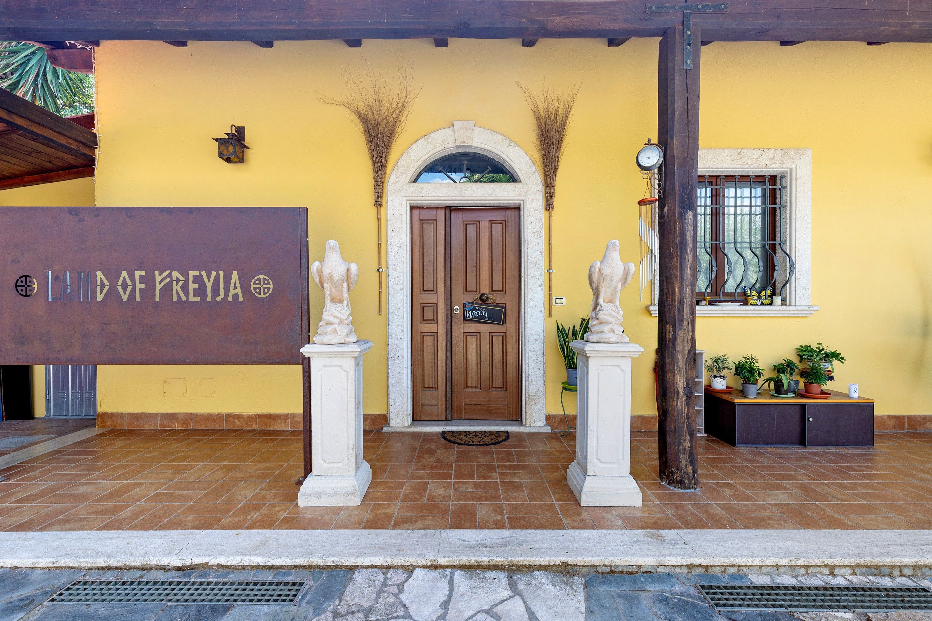 A building entrance with a wooden door, two white statues, a sign reading 'LAND OF PREYJA', and a window with a metal grill.