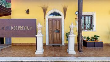 A building entrance with a wooden door, two white statues, a sign reading 'LAND OF PREYJA', and a window with a metal grill.