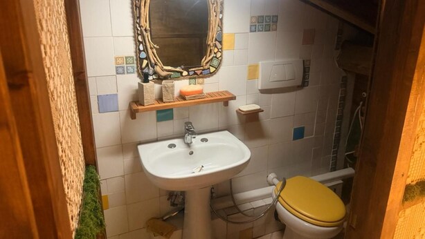 A bathroom with a white sink, a mirror with a decorative frame, a toilet with a yellow seat, and a shower area. - Room 'Terra' with shared pool, Wi-Fi and air conditioning (Santa Marinella)
