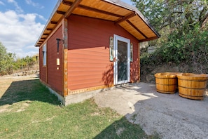 A small wooden cabin with a sloped roof, a glass door, and two wooden barrels outside.