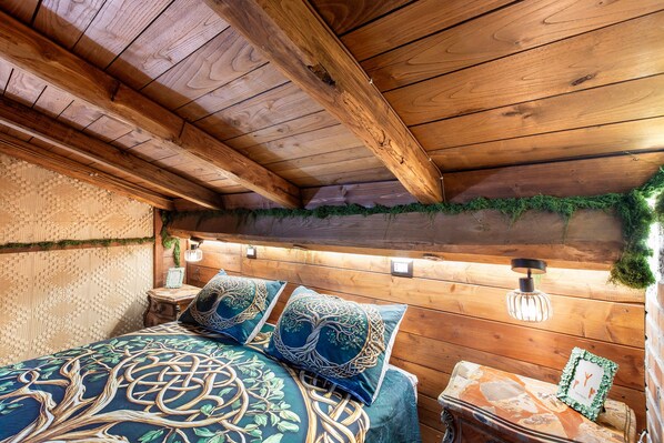 A rustic wooden room with a bed, a nightstand, and a wall-mounted light fixture.