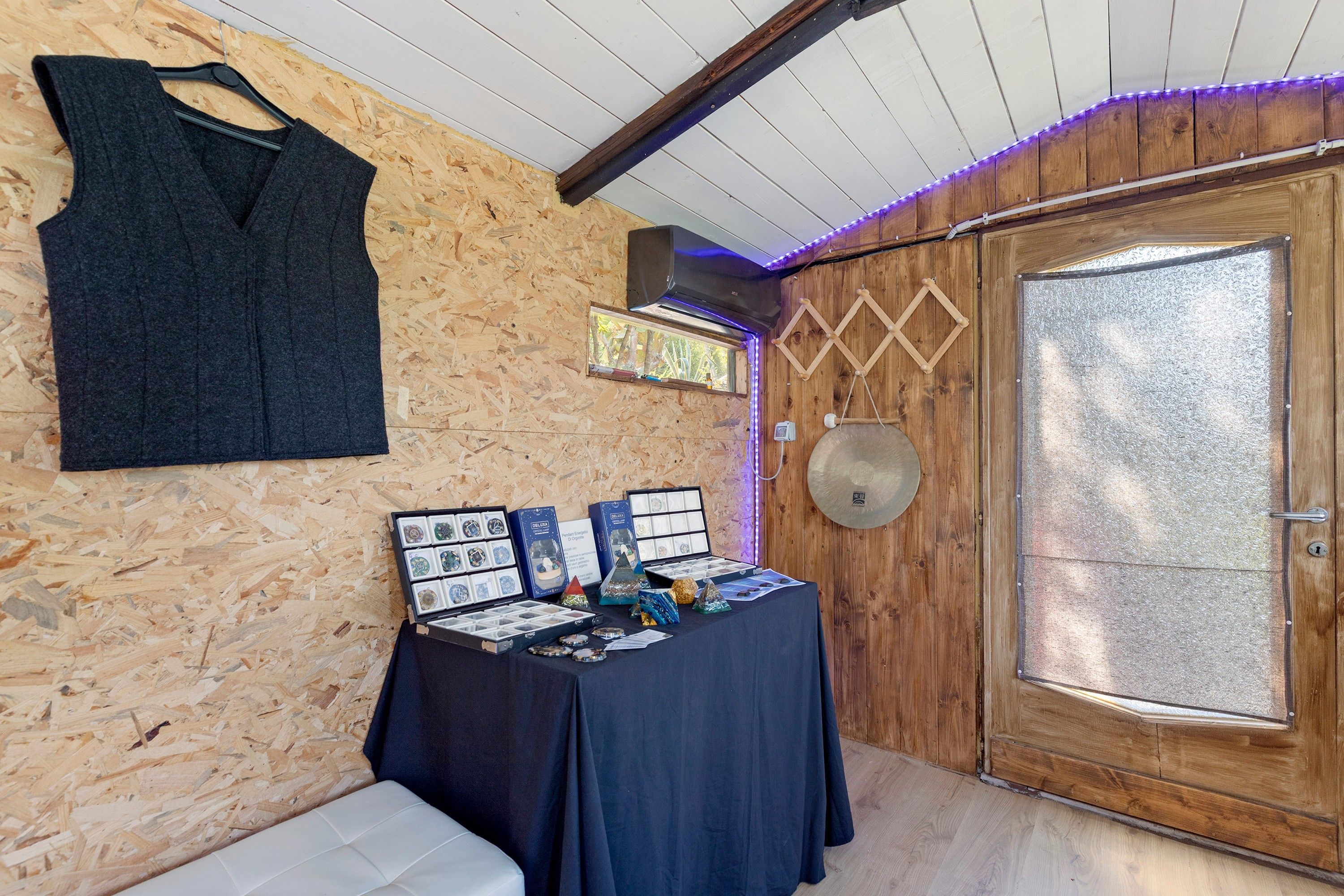 A room with a wooden wall, a table with crystal displays, a hanging garment, and a door with a frosted glass panel.