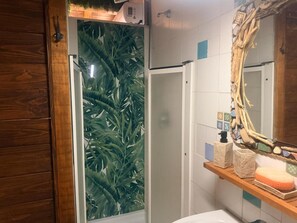 Un bagno con doccia, un mobile bagno in legno, uno specchio e una parete rivestita di piastrelle.