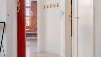 A hallway with a wooden floor, a red pillar, and a door leading to a room with a brick wall.