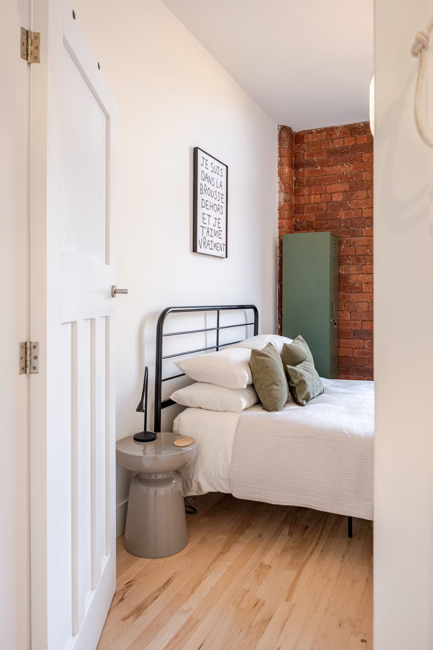 A bedroom with a bed, a bedside table, a wall-mounted picture, and a brick wall.