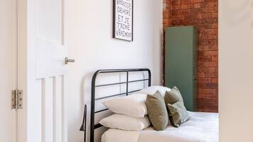 A bedroom with a bed, a bedside table, a wall-mounted picture, and a brick wall.
