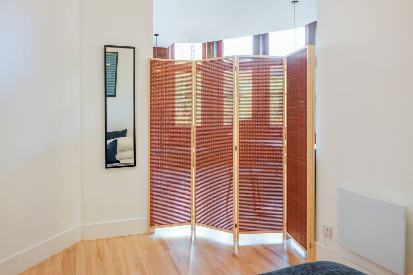A room with a wooden floor, a framed picture on the wall, and a room divider.
