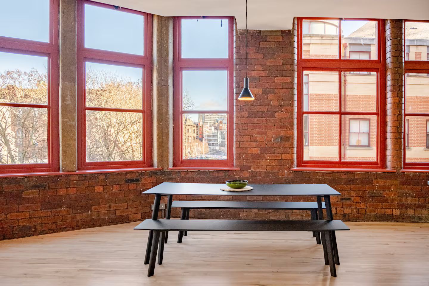 A room with a large table, red-framed windows, and a hanging light fixture.
