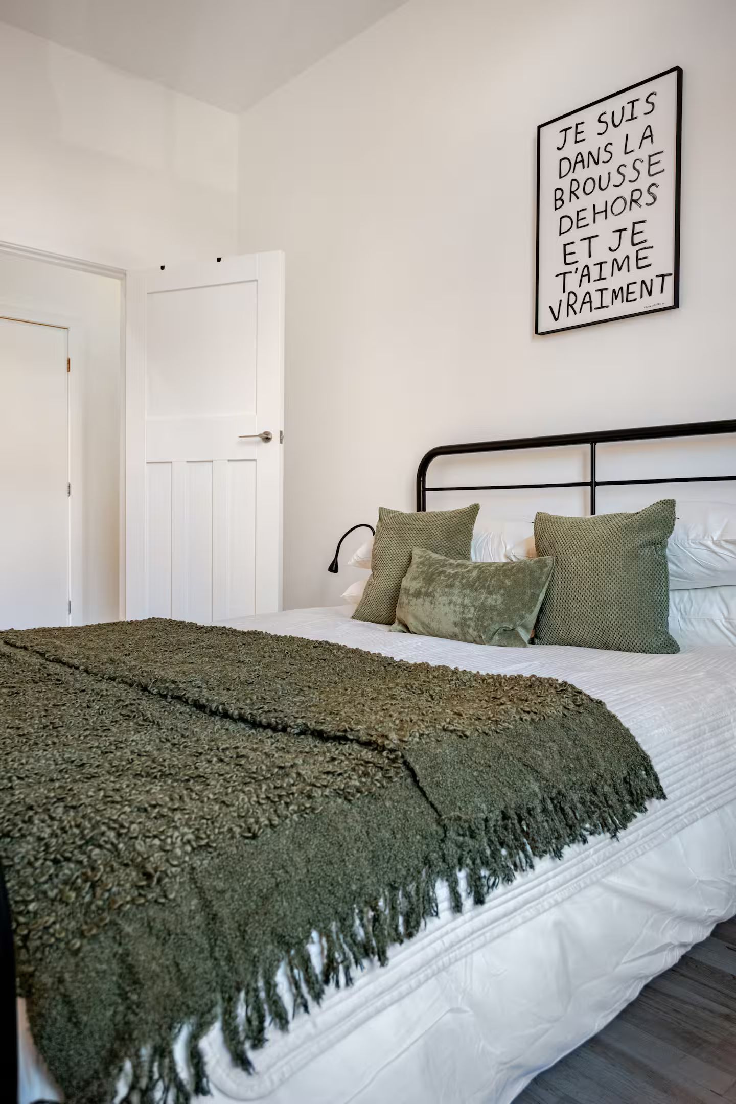 Un dormitorio con cama, almohadas, una colcha y un cartel en la pared.