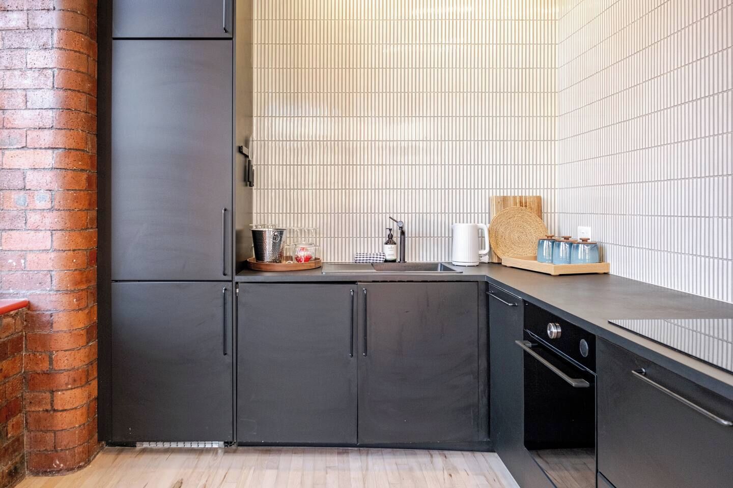 A modern kitchen with dark cabinetry, a brick column, and a tiled backsplash.