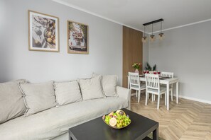 A living room with a sofa, a dining table with chairs, a black coffee table with a fruit bowl, and two framed pictures on the wall. - Lumina comfy apart center of Warsaw  (Warszawa)