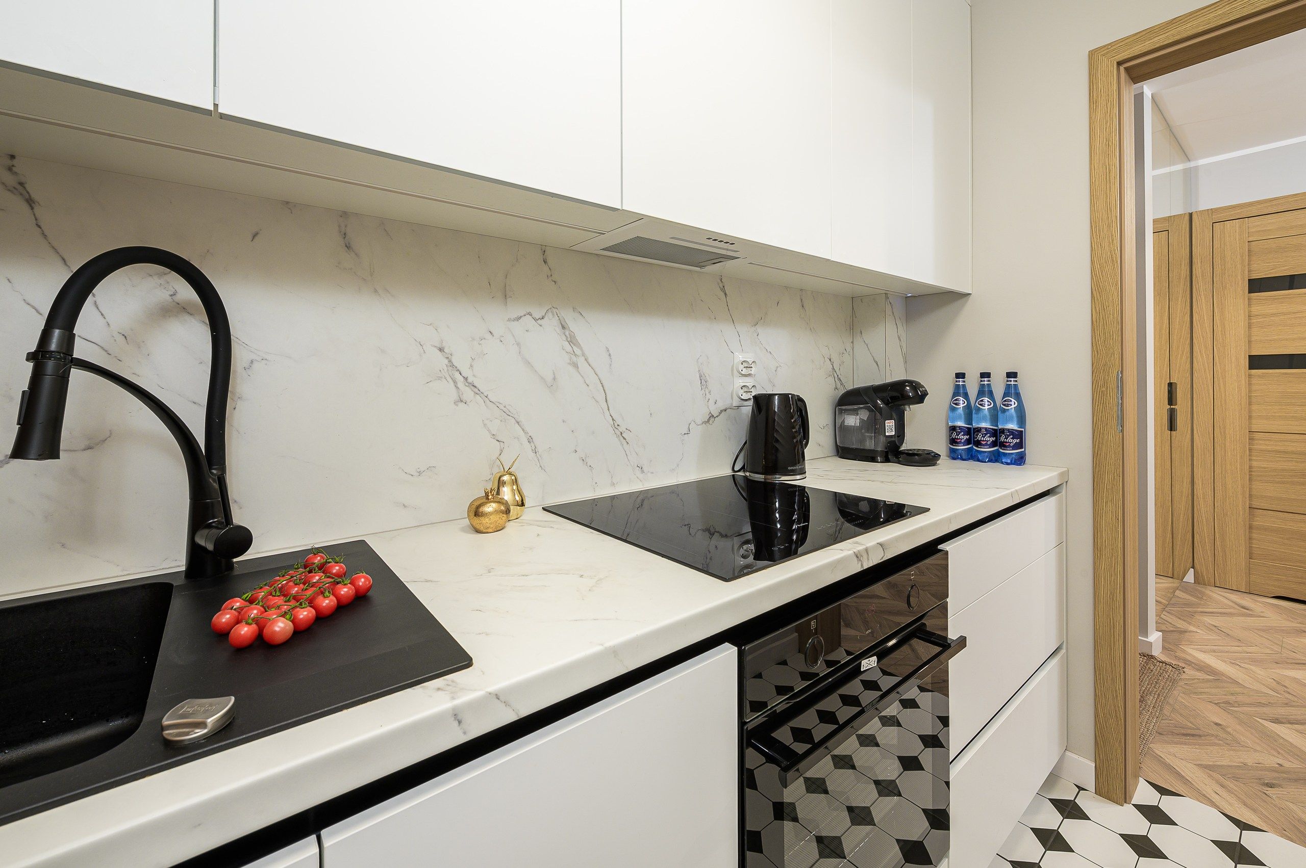 A modern kitchen with a black faucet, a black induction cooktop, a white marble countertop, and a black and white patterned floor.