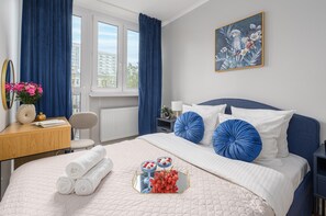 Une chambre d’hôtel avec un lit, un bureau, une chaise, un radiateur, une fenêtre avec des rideaux et un tableau au mur.