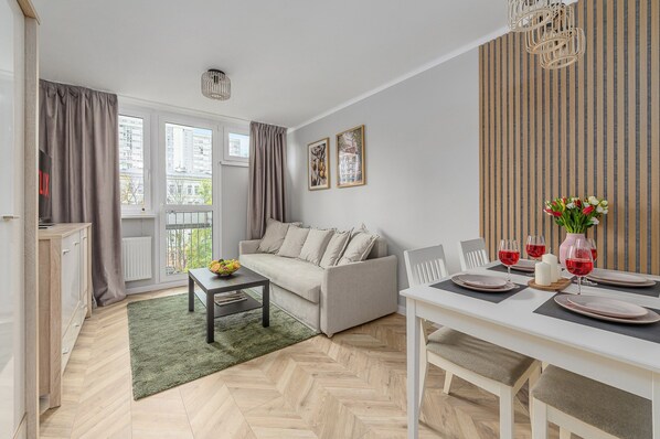 Un salon moderne avec un canapé, une table à manger et une vue sur la ville grâce à de grandes fenêtres.