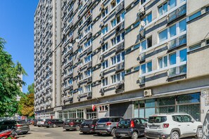 Um edifício residencial com várias andares, varandas, grandes janelas e carros estacionados em frente.