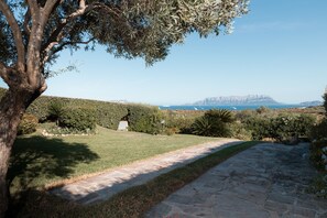 A stone pathway leading to a grassy area with a view of the sea and distant mountains. - Villetta Rosella by Wonderful Italy (Golfo Aranci)