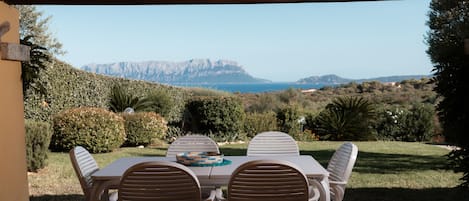 An outdoor patio with a table and chairs, overlooking a mountainous landscape and the sea.