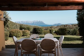 Um pátio externo com mesa e cadeiras, com vista para uma paisagem montanhosa e o mar.