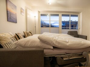 A bedroom with a bed, a chair, a window with blinds, and artwork on the wall. - 6 in the Pole Poppenspaler House (St. Peter-Ording)