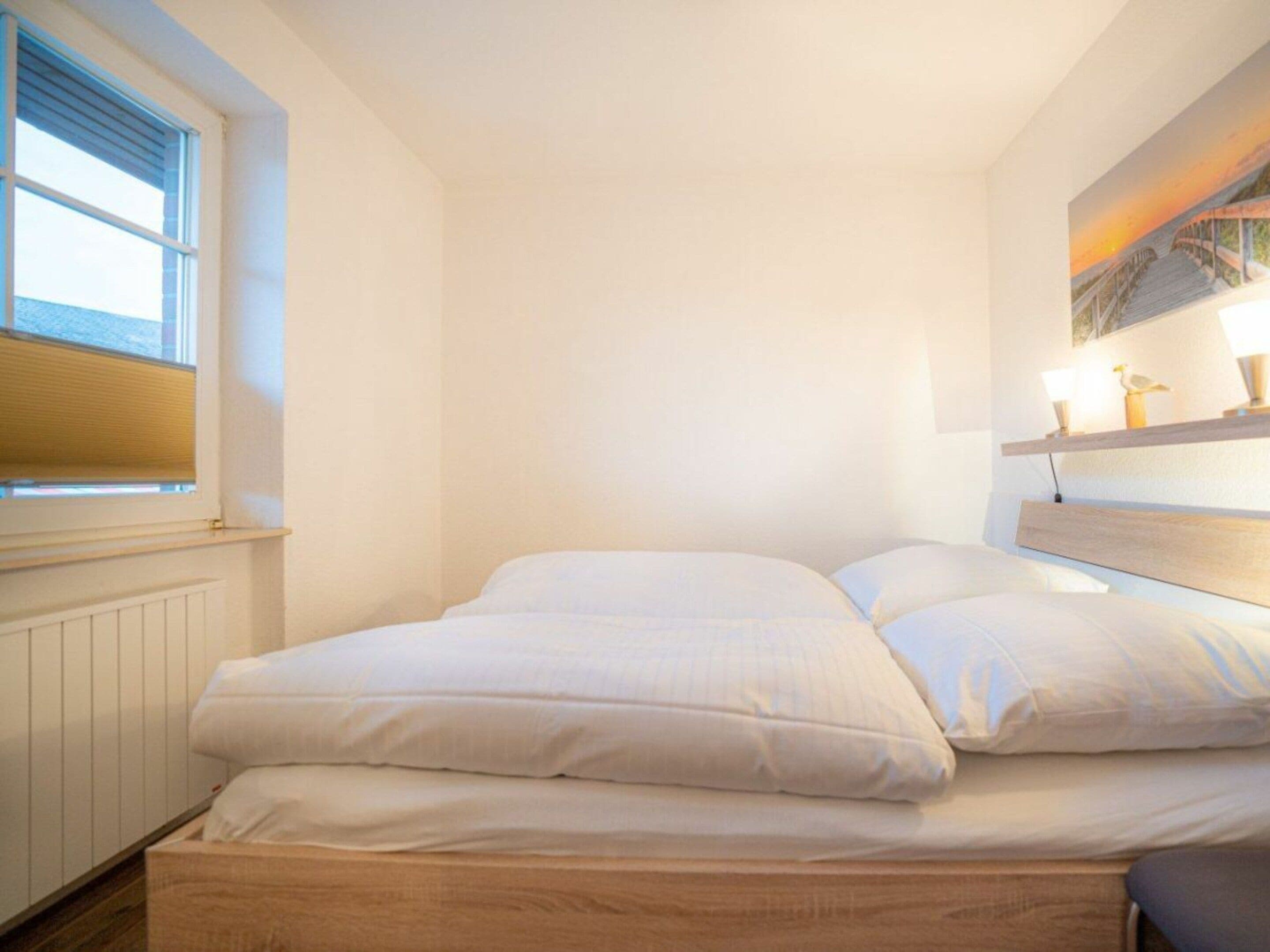 A bedroom with a bed, a window, and a shelf with decorative items.