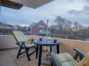 A balcony with two chairs and a small round table, a metal railing, and a view of buildings and trees. - 6 in the Pole Poppenspaler House (St. Peter-Ording)