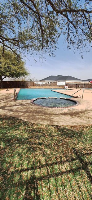 A backyard with a swimming pool, a hot tub, and a wooden fence.