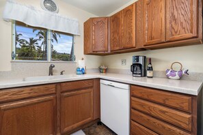 A kitchen with wooden cabinets, a coffee maker, a wine bottle, and a teapot. - Keauhou Palena #604 – Peaceful 1 Bedroom, 2 Bath Kona Retreat with A/C (KAILUA-KONA)
