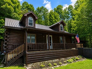 A log cabin with a porch, a flag, and a stone pathway.