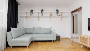Ein modernes Wohnzimmer mit einem hellgrauen Ecksofa, Holzboden und weißen Wänden.
