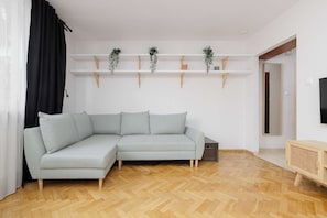 Una sala de estar moderna con un sofá seccional de color gris claro, piso de madera y paredes blancas.