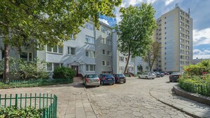 Eine Wohnstraße mit parkenden Autos, einem grünen Zaun und mehrstöckigen Gebäuden.