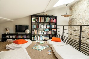 Une chambre avec deux lits, une bibliothèque, un téléviseur et un mur en pierre.