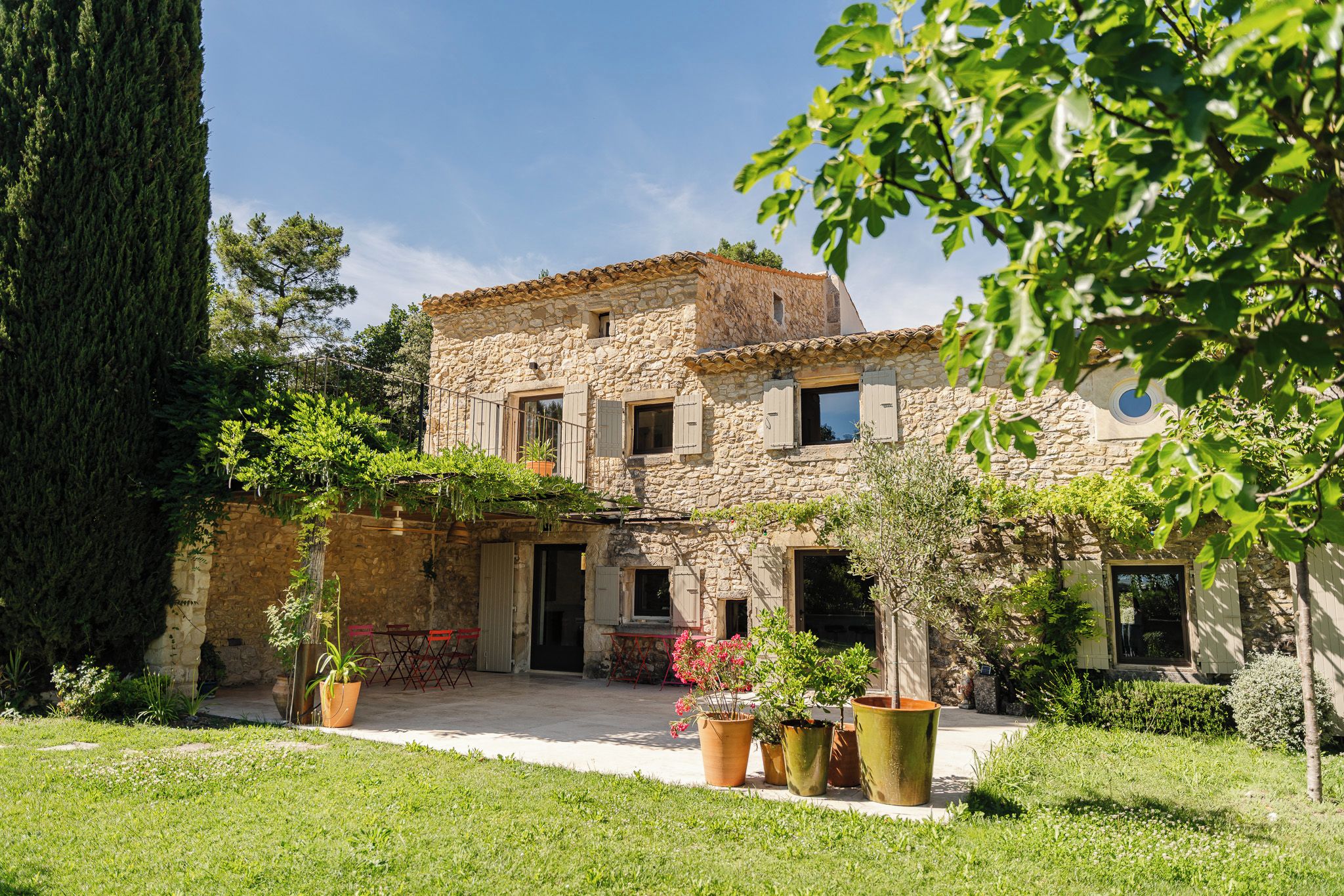 A stone building with a tiled roof, a covered patio, and potted plants.