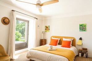 Ein Schlafzimmer mit einem Bett, einem Deckenventilator, einem Fenster mit Vorhängen, einem Nachttisch und einer Lampe.