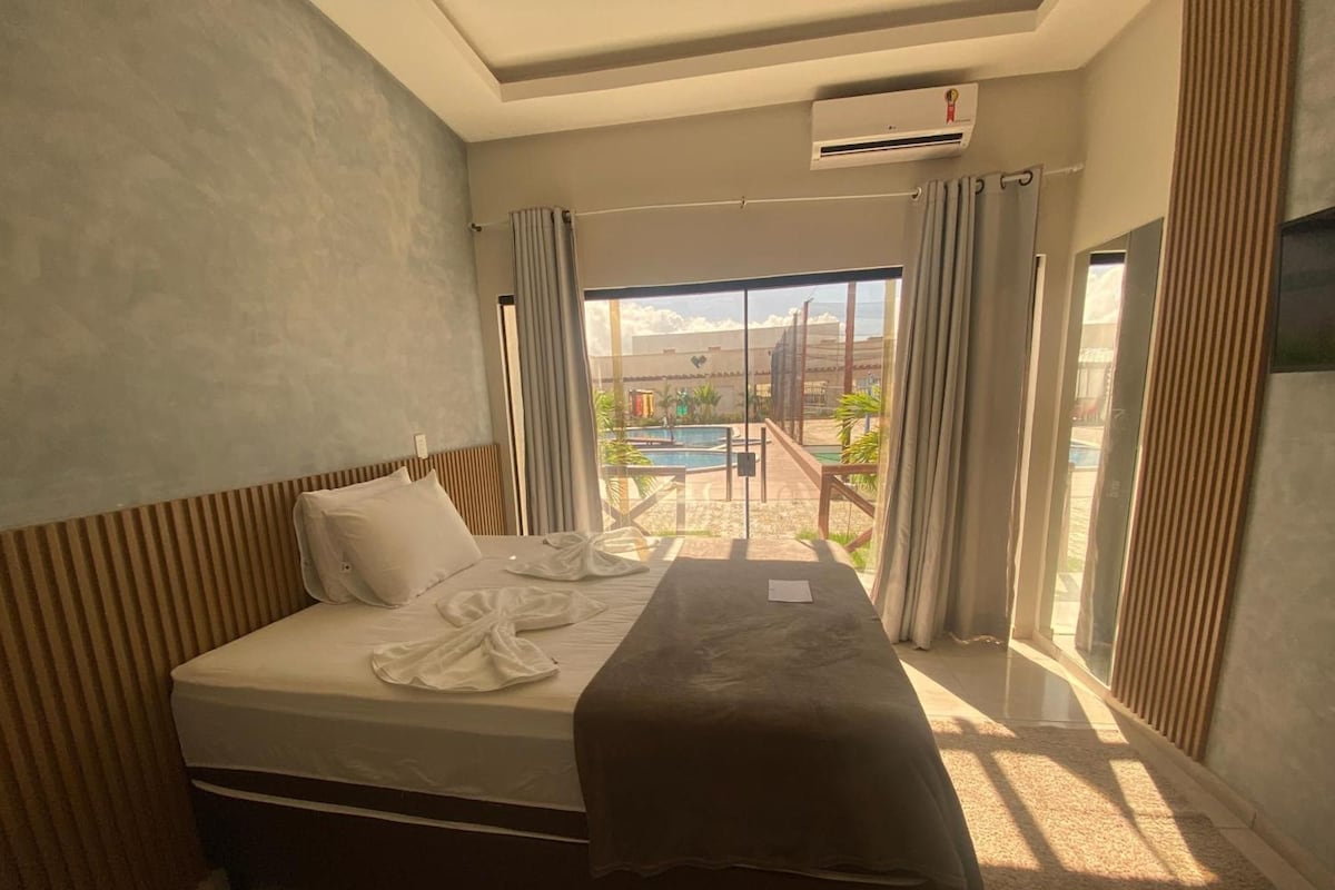 A hotel room with a bed, a window, and an air conditioning unit.