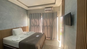 Ett hotellrum med en säng, en platt-TV som är monterad på väggen och ett fönster med gardiner.