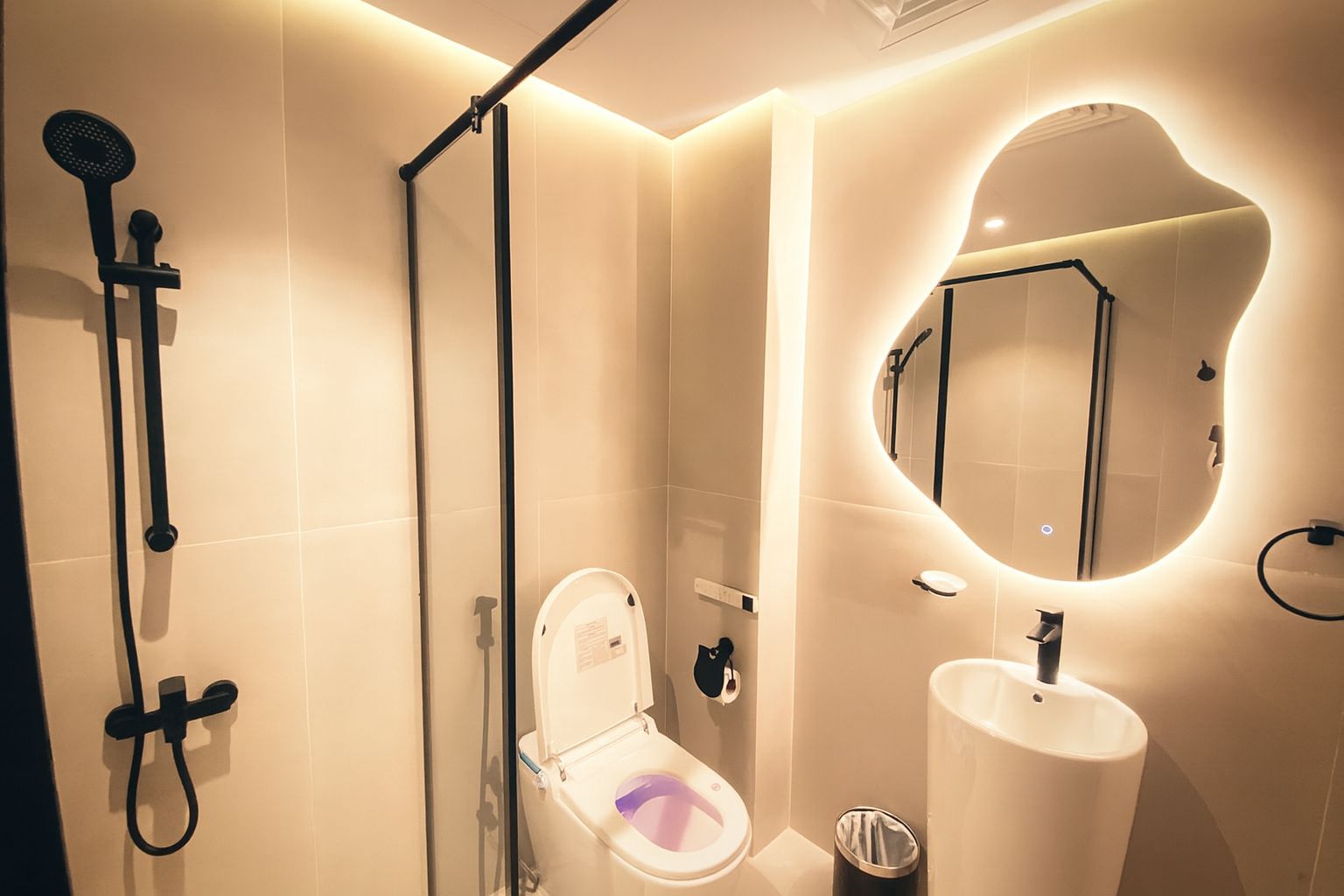 Un baño moderno con cabina de ducha de vidrio, inodoro y lavamanos con espejo.