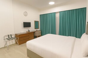 Ett hotellrum med en säng, ett skrivbord med en stol, en tv och ett fönster med gardiner.