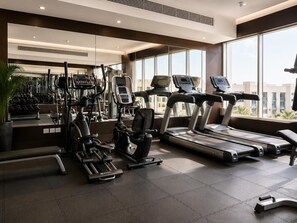 A modern gym with various exercise equipment, large windows, and a view of buildings. - City Stay DubaiSouth-Serviced Apartments (Dubai)