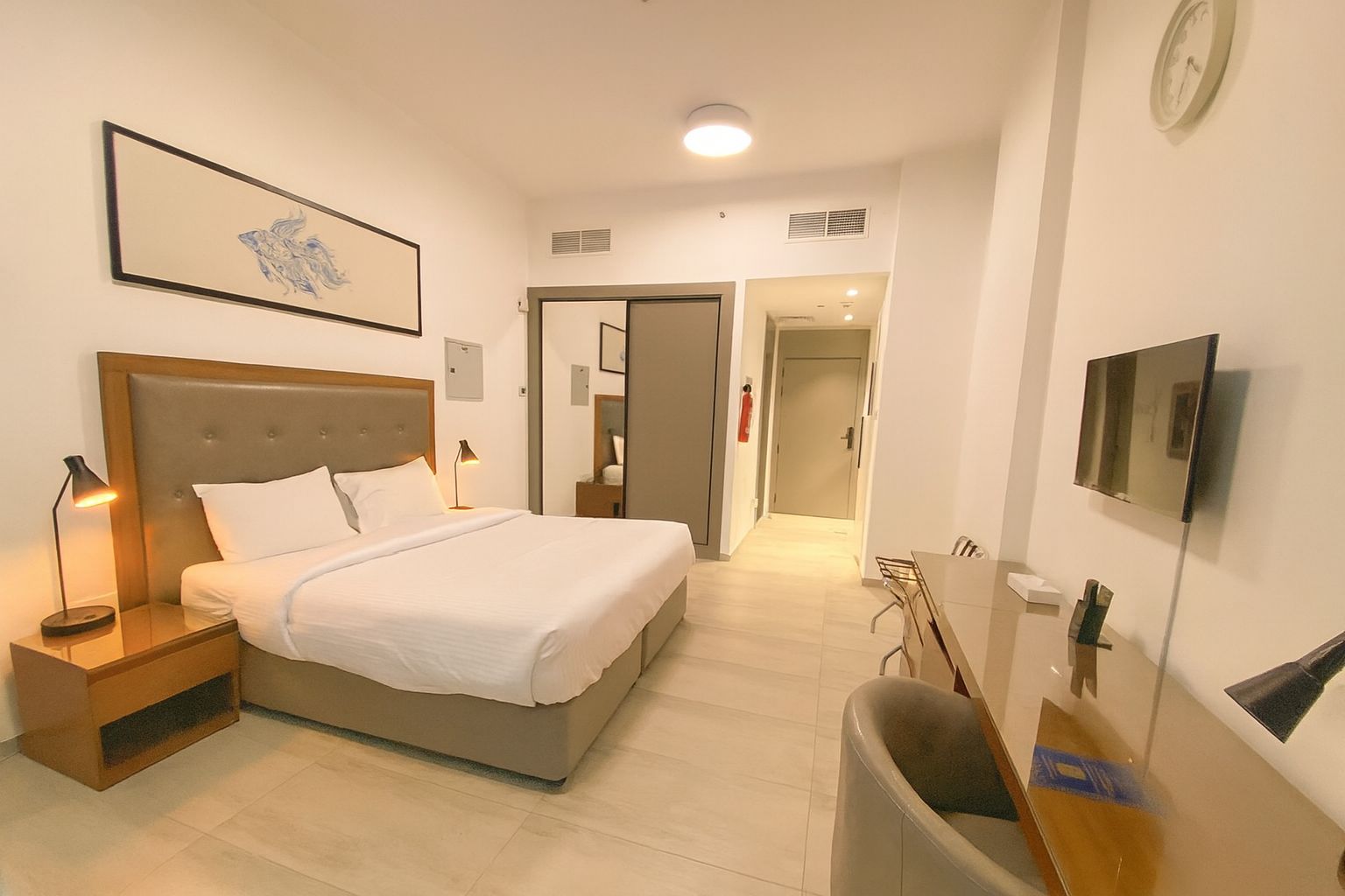 Habitación de hotel con cama, mesitas de noche, escritorio, silla, televisor y un cuadro en la pared.