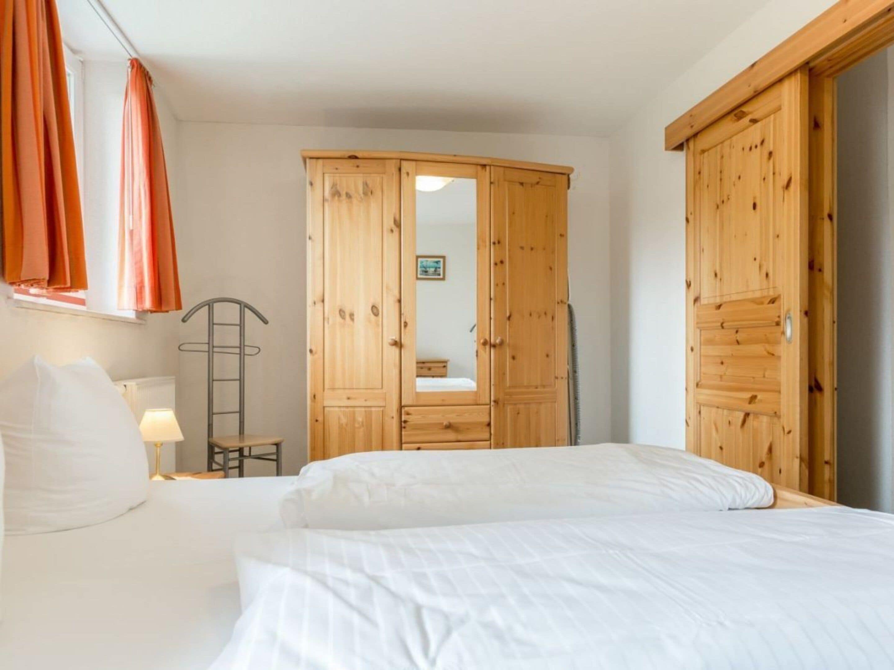 Quarto com cama, guarda-roupa de madeira, espelho e radiador.