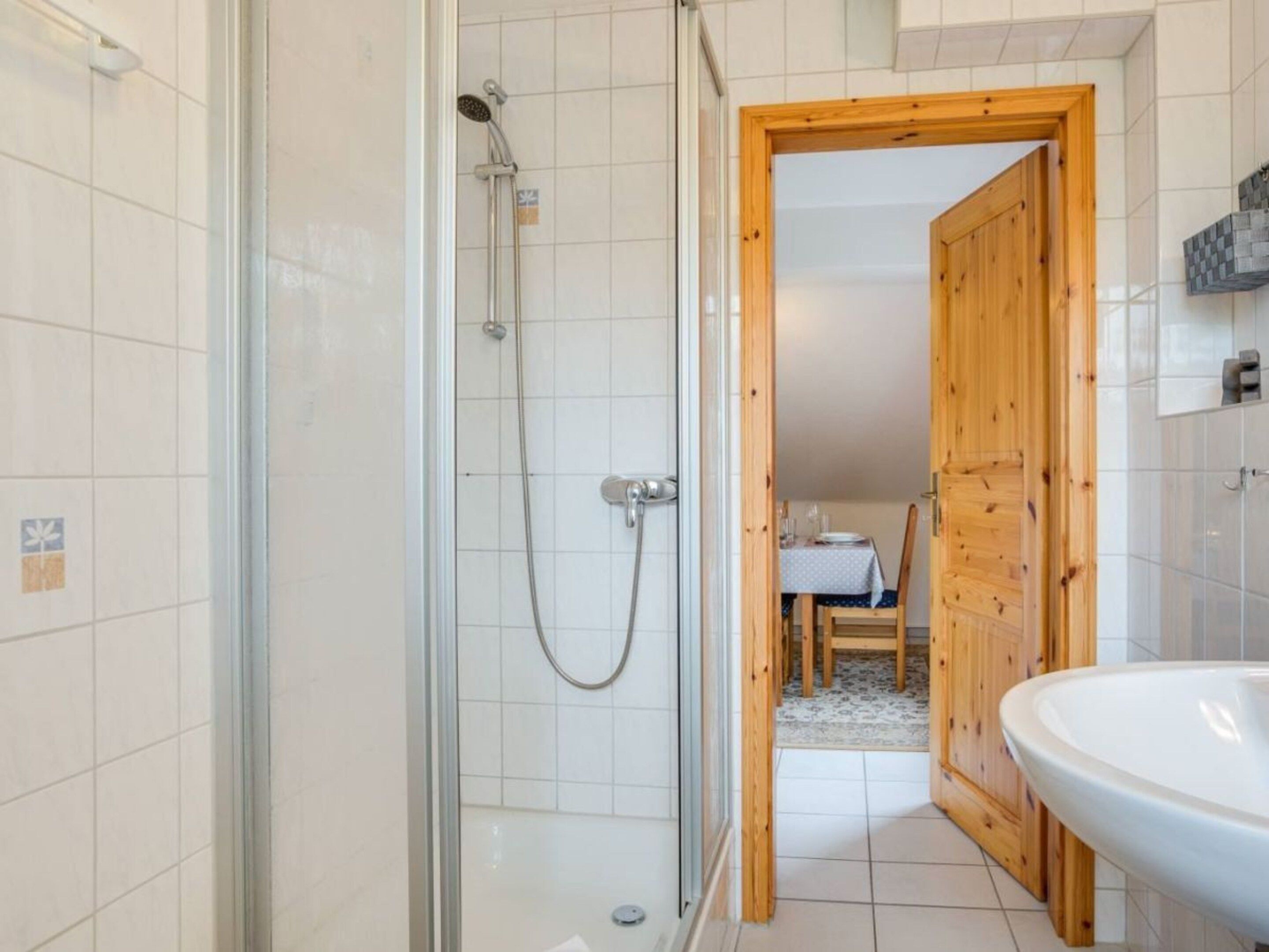 Ein Badezimmer mit einer gläsernen Duschkabine, einer Holztür zu einem Essbereich und einem weißen Waschbecken.