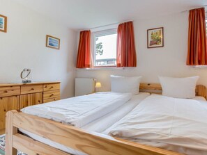 A room with a bed, a bedside table, a lamp, a window with curtains, and a picture on the wall. - 5 in the House Sturmmowe (St. Peter-Ording)